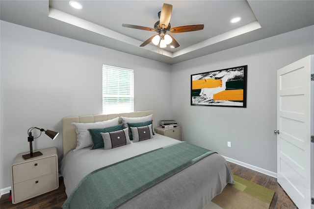 bedroom with ceiling fan, dark wood-type flooring, and a tray ceiling