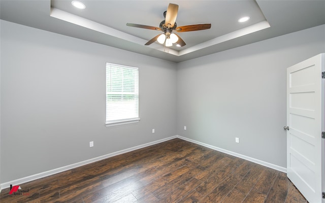 empty room with a tray ceiling, ceiling fan, and dark wood-type flooring