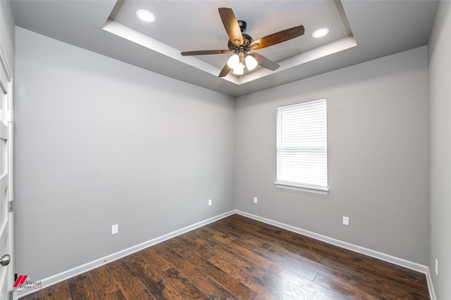 unfurnished room featuring a raised ceiling, ceiling fan, and dark hardwood / wood-style flooring