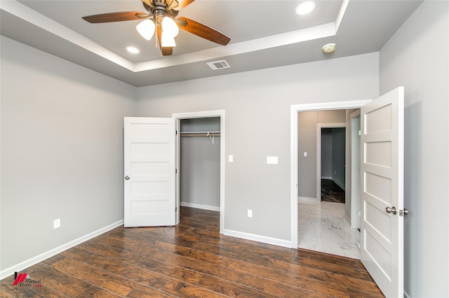 unfurnished bedroom featuring a closet, ceiling fan, a tray ceiling, and dark hardwood / wood-style floors