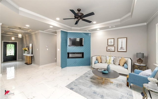 living room featuring a large fireplace, a raised ceiling, ceiling fan, and crown molding