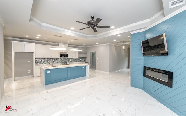 kitchen with hanging light fixtures, wood walls, a center island with sink, white cabinets, and ornamental molding