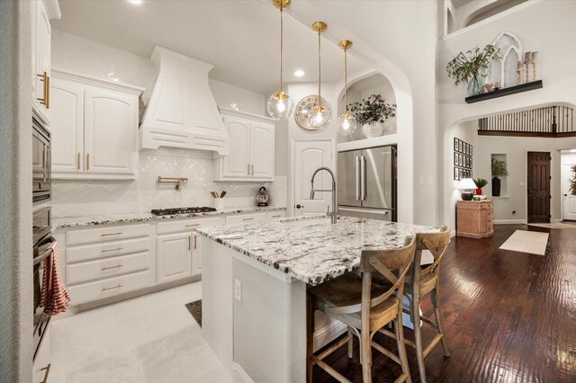 kitchen featuring appliances with stainless steel finishes, custom exhaust hood, white cabinets, and a center island with sink