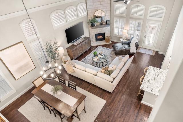 living room with ceiling fan with notable chandelier, a towering ceiling, dark hardwood / wood-style flooring, and a stone fireplace