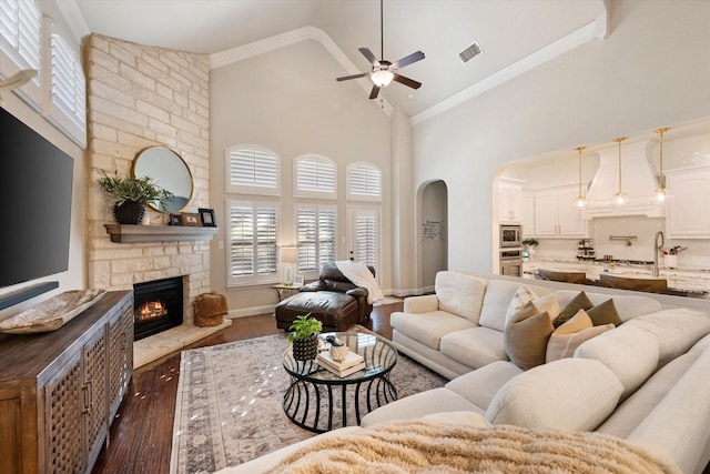 living room featuring dark hardwood / wood-style floors, high vaulted ceiling, crown molding, a fireplace, and ceiling fan