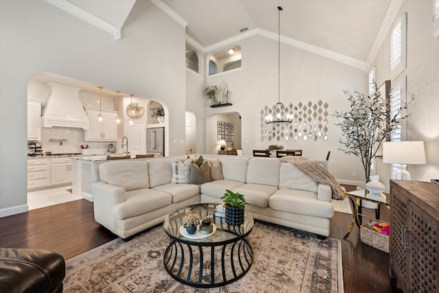 living room featuring dark wood-type flooring, an inviting chandelier, high vaulted ceiling, crown molding, and sink