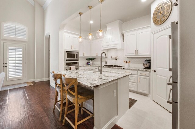 kitchen featuring white cabinets, premium range hood, and an island with sink