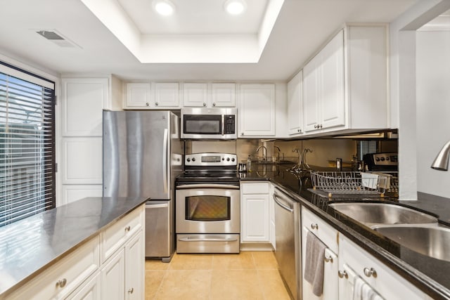 kitchen with appliances with stainless steel finishes, dark stone counters, a raised ceiling, sink, and white cabinetry