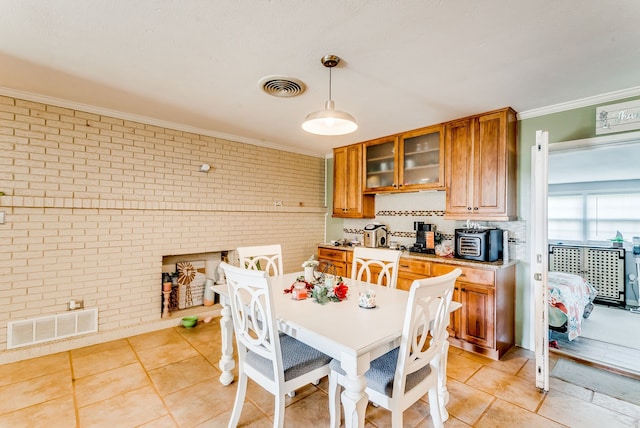 kitchen with light tile patterned floors, hanging light fixtures, crown molding, and brick wall