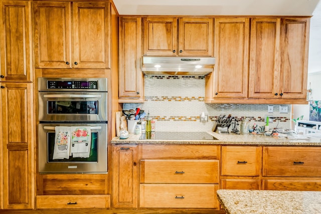 kitchen with light stone counters, stainless steel double oven, black electric cooktop, and tasteful backsplash