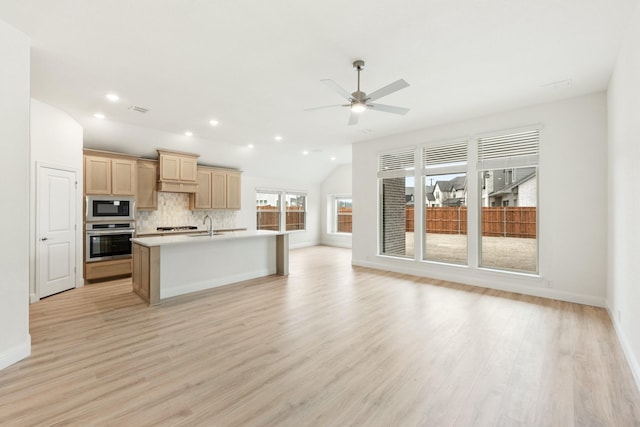 kitchen featuring appliances with stainless steel finishes, tasteful backsplash, light stone counters, sink, and an island with sink