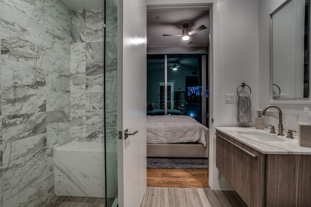 bathroom with hardwood / wood-style flooring, ceiling fan, a tile shower, and vanity