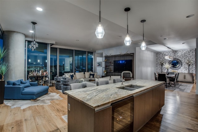 kitchen featuring a kitchen island with sink, sink, light stone countertops, light wood-type flooring, and beverage cooler