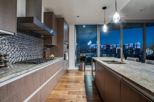 kitchen with light stone countertops, sink, wall chimney exhaust hood, light hardwood / wood-style flooring, and stainless steel gas stovetop