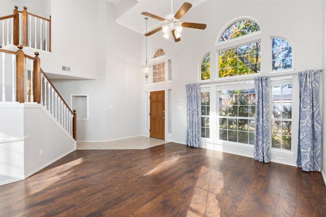 unfurnished living room with ceiling fan, a towering ceiling, and dark hardwood / wood-style floors