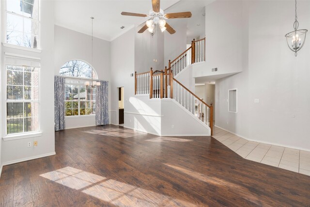 unfurnished living room featuring dark wood-type flooring, a towering ceiling, and ceiling fan with notable chandelier