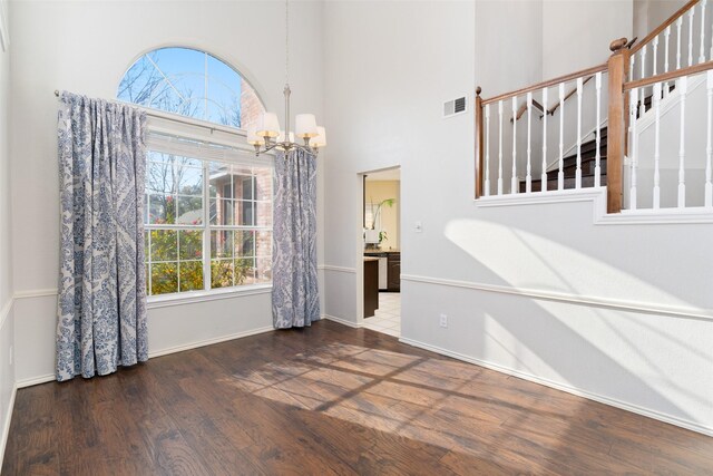 spare room with dark wood-type flooring, a chandelier, and a towering ceiling