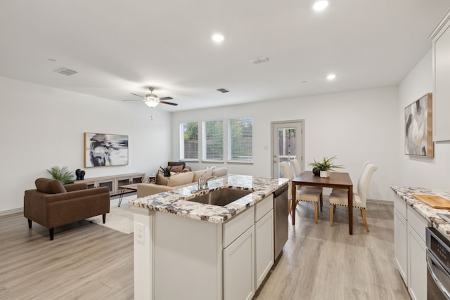 kitchen with light stone countertops, appliances with stainless steel finishes, sink, a center island with sink, and light hardwood / wood-style flooring