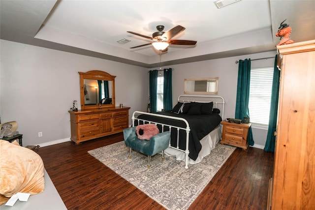 bedroom with ceiling fan, dark wood-type flooring, a tray ceiling, and multiple windows