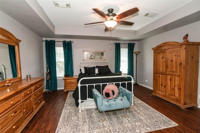 bedroom with a tray ceiling, ceiling fan, and dark wood-type flooring