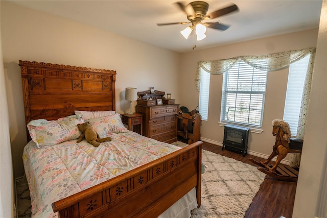 bedroom with ceiling fan, dark hardwood / wood-style flooring, and a wood stove