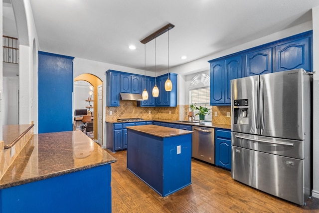 kitchen with a kitchen island, appliances with stainless steel finishes, pendant lighting, blue cabinets, and dark hardwood / wood-style flooring