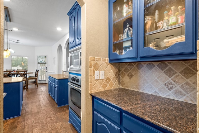 kitchen featuring blue cabinetry, dark wood-type flooring, decorative light fixtures, stainless steel appliances, and backsplash