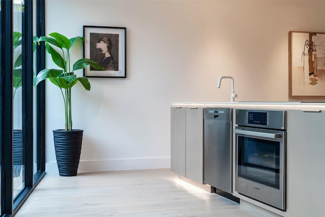 bar featuring stainless steel oven, sink, and light hardwood / wood-style flooring