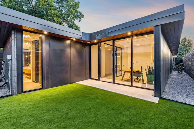 back house at dusk featuring a patio area and a yard