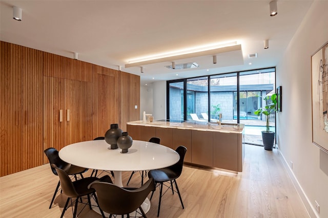 dining area with light hardwood / wood-style flooring, a wall of windows, and wooden walls