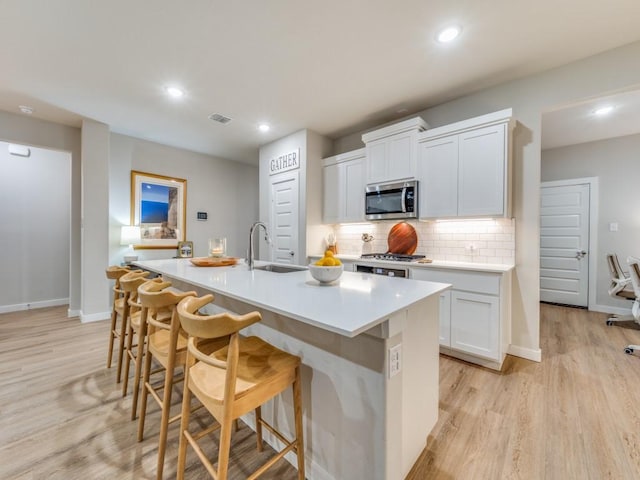 kitchen featuring stainless steel appliances, white cabinets, and an island with sink