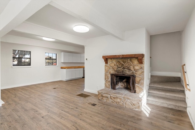 unfurnished living room with a fireplace, beam ceiling, and light hardwood / wood-style floors