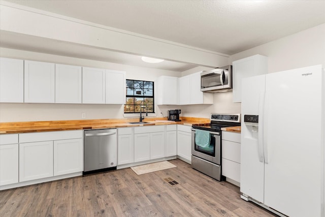 kitchen with wooden counters, appliances with stainless steel finishes, light wood-type flooring, sink, and white cabinets