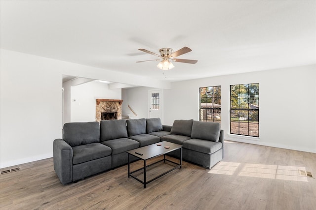 living room featuring a stone fireplace, ceiling fan, and wood-type flooring