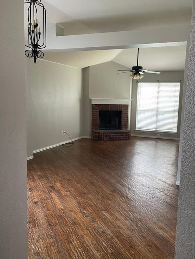 unfurnished living room featuring dark hardwood / wood-style floors, lofted ceiling, ceiling fan with notable chandelier, and a brick fireplace