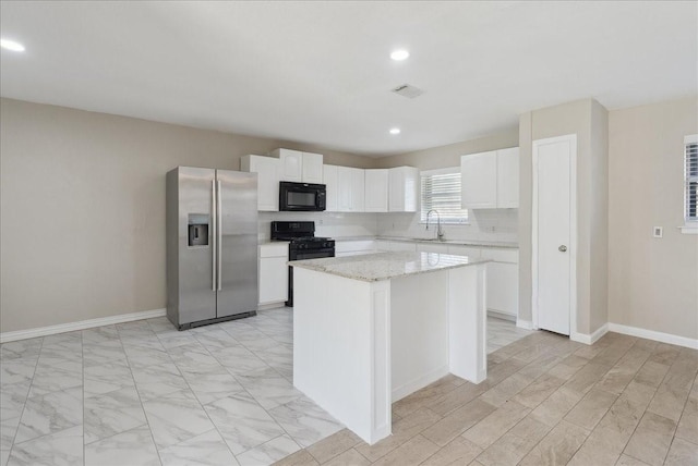 kitchen with light stone countertops, white cabinetry, sink, a center island, and black appliances