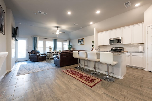 kitchen featuring light stone countertops, stainless steel appliances, light hardwood / wood-style flooring, a breakfast bar area, and white cabinets