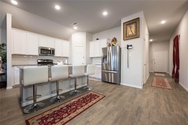 kitchen with a breakfast bar, stainless steel appliances, a kitchen island with sink, wood-type flooring, and white cabinetry