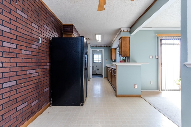 kitchen featuring black fridge with ice dispenser, a textured ceiling, ornamental molding, ceiling fan, and brick wall