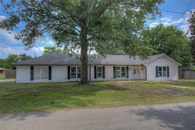 ranch-style home with roof with shingles, a front lawn, and fence