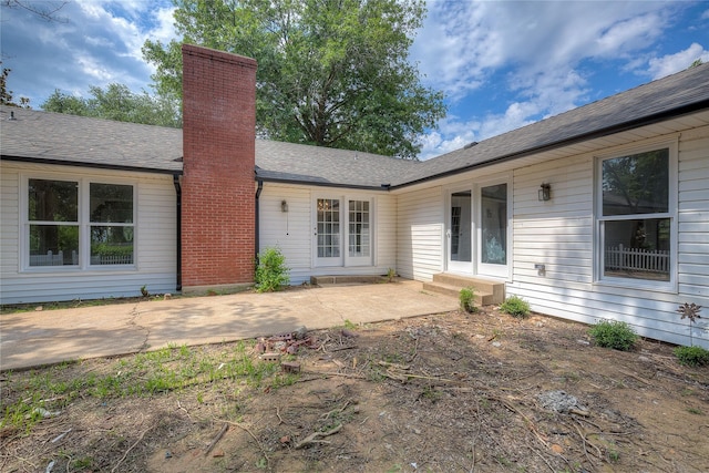 back of house with entry steps, a patio, a shingled roof, and a chimney