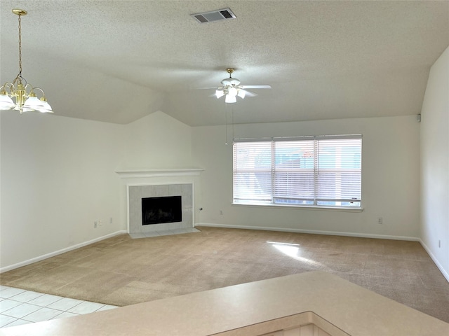 unfurnished living room featuring vaulted ceiling, light carpet, a tiled fireplace, a textured ceiling, and ceiling fan with notable chandelier