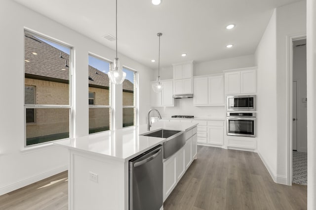 kitchen featuring a kitchen island with sink, white cabinets, sink, decorative light fixtures, and stainless steel appliances