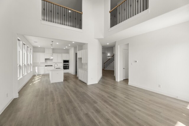 unfurnished living room with light wood-type flooring, a towering ceiling, and sink