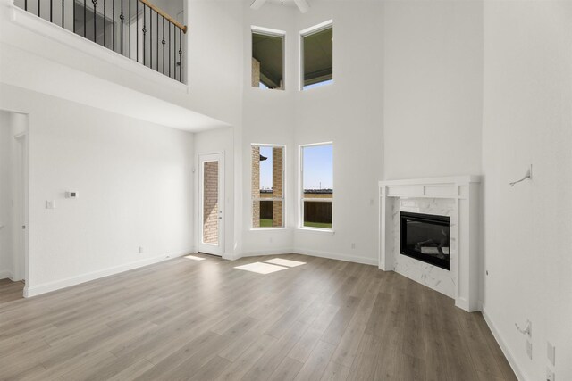 unfurnished living room featuring ceiling fan, a high end fireplace, a towering ceiling, and hardwood / wood-style flooring