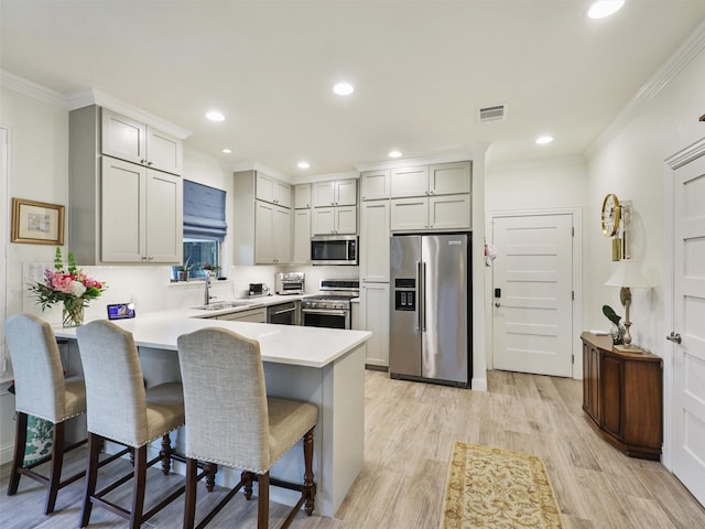 kitchen featuring kitchen peninsula, a kitchen breakfast bar, ornamental molding, stainless steel appliances, and light hardwood / wood-style flooring