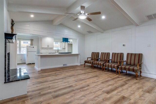 living room with ceiling fan, sink, vaulted ceiling with beams, light hardwood / wood-style flooring, and a fireplace