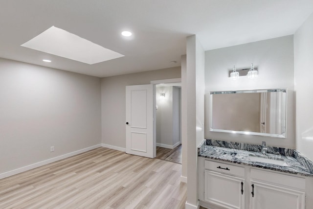 bathroom featuring a skylight, baseboards, wood finished floors, vanity, and recessed lighting