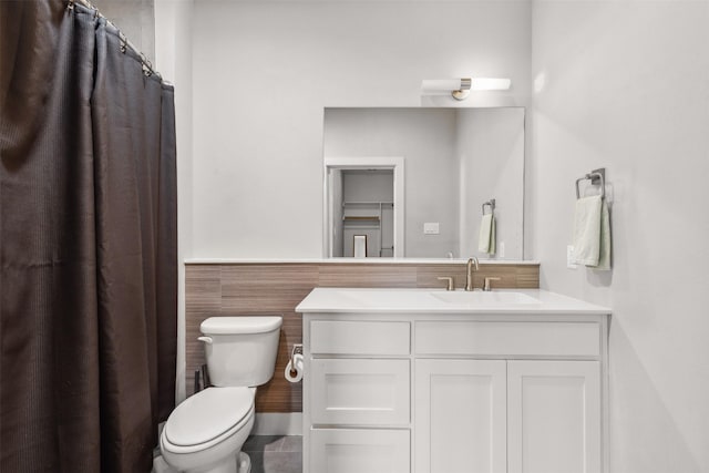 bathroom featuring toilet, wainscoting, tile walls, and vanity