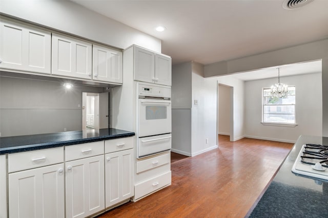 kitchen with hardwood / wood-style flooring, a notable chandelier, white cabinetry, and white appliances